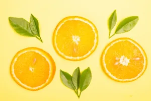 Bright orange slices and green leaves on a yellow background create a vivid citrus-themed flat lay. jigsaw puzzle