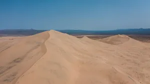 Expansive sand dunes in a remote desert region under a bright blue sky, showcasing natural beauty. jigsaw puzzle