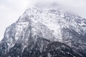 A stunning view of a snow-covered mountain peak enveloped in clouds, captured during winter. jigsaw puzzle