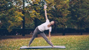 A woman performs yoga on a mat in a scenic park with colorful autumn trees. jigsaw puzzle