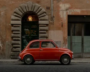 A classic red car parked against an old stone building, evoking a retro urban charm. jigsaw puzzle