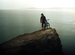 a man standing on top of a cliff next to a bike jigsaw puzzle