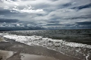 A dramatic view of a sandy beach with stormy clouds and waves crashing on the shore. jigsaw puzzle