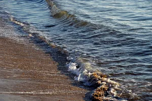 Gentle ocean waves roll onto a sandy beach at sunset, capturing a peaceful coastal scene. jigsaw puzzle
