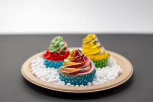 Colorful cupcakes with swirled icing on a paper plate surrounded by small white balls. jigsaw puzzle