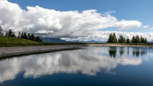 A tranquil lake in the countryside reflecting dramatic clouds and trees under a bright sky. jigsaw puzzle