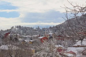 Idyllic snow-laden village nestled amidst winter forest and hills, creating a serene scene. jigsaw puzzle