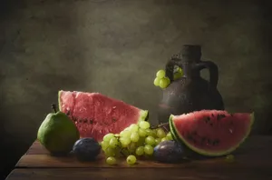 A classic still life featuring watermelon, grapes, pear, plums, and rustic pottery on a wooden table. jigsaw puzzle