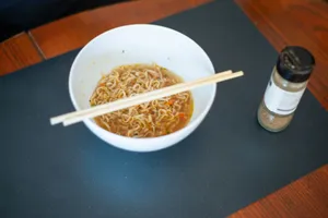 A bowl of steaming Asian noodles with chopsticks, set on a table, inviting a delicious meal experience. jigsaw puzzle