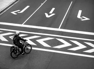 Black and white photo of a cyclist on an urban road with clear directional markings in Vancouver. jigsaw puzzle