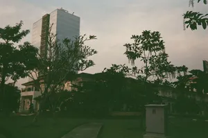 A towering highrise stands amidst lush greenery and trees, captured at dusk, showcasing urban architecture. jigsaw puzzle