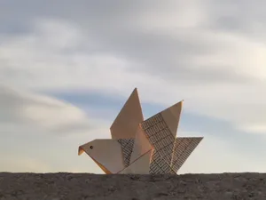 Origami bird resting on a surface with a serene blue sky in the background, minimalistic composition. jigsaw puzzle