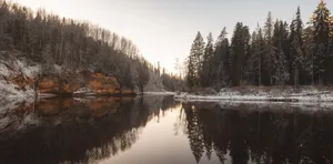 Calm river reflecting snow-dusted trees and rocky bank. jigsaw puzzle