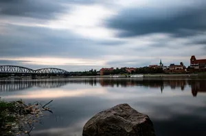 Peaceful riverside landscape featuring a historic bridge, town skyline, and calm waters reflecting the sky. jigsaw puzzle