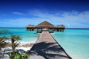 Scenic view of a wooden boardwalk leading to serene overwater bungalows at an island resort. jigsaw puzzle