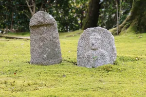 Two ancient stone statues surrounded by lush green moss, capturing the serene beauty of a Kyoto garden. jigsaw puzzle