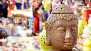 Close-up of a Buddha statue at an outdoor market with vibrant background. jigsaw puzzle