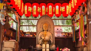 A peaceful Buddha statue surrounded by red lanterns and offerings in a traditional Japanese setting. jigsaw puzzle