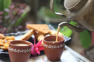 A warm cup of tea being poured from a kettle, surrounded by snacks and a flower. jigsaw puzzle