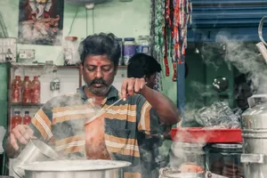 A man making traditional masala chai in an Indian tea stall, surrounded by steam and kitchen utensils. jigsaw puzzle