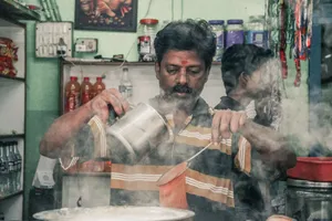 A man pouring hot masala chai with steam rising, capturing a traditional Indian market scene. jigsaw puzzle