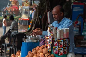 Street vendor in blue shirt serving chai in clay cups at a bustling outdoor market. jigsaw puzzle