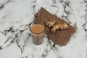 A glass of traditional Indian masala chai served with fresh ginger on a marble countertop. jigsaw puzzle