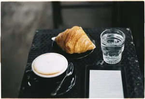 A peaceful coffee break with a croissant, cappuccino, and e-reader on a café table. jigsaw puzzle