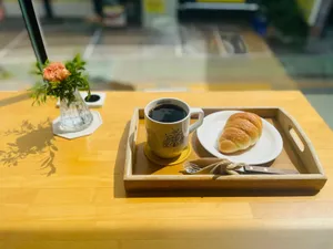 A warm, inviting café setting featuring coffee, a croissant, and a flower vase on a sunny wooden table. jigsaw puzzle