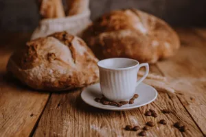 Artistic arrangement of fresh bread and a coffee cup on a rustic wooden table with scattered coffee beans. jigsaw puzzle