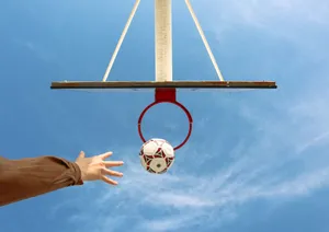 Unique angle capturing a soccer ball nearing a basketball hoop against a bright blue sky. jigsaw puzzle