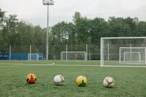 Four soccer balls on an outdoor field near goalposts, ideal for sports themes. jigsaw puzzle