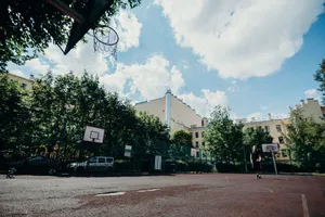 An outdoor basketball court in the city with clear skies, trees, and buildings. jigsaw puzzle