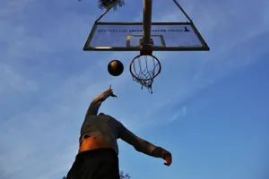 Athlete jumping to shoot a basketball with clear blue sky backdrop, captured from a low angle. jigsaw puzzle
