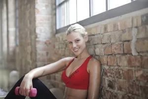 Blonde woman in red sportswear smiling with a dumbbell in a bright gym setting. jigsaw puzzle