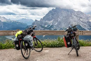 Two touring bicycles with luggage parked against a scenic mountain backdrop under cloudy skies. jigsaw puzzle