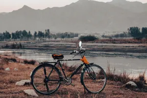 A tranquil view of a vintage bicycle by a serene mountain range and river at twilight. jigsaw puzzle