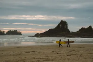 Two surfers with boards walk along a tranquil beach as the sun sets over the ocean. jigsaw puzzle