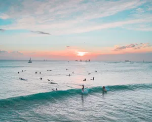 A picturesque scene of surfers riding waves at sunset on a tropical beach, with a vibrant sky creating a serene atmosphere. jigsaw puzzle