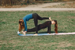 Side view of fit lady in sports clothes standing in Phalakasana pose and supporting slim unrecognizable girlfriend on mat in park in daylight jigsaw puzzle