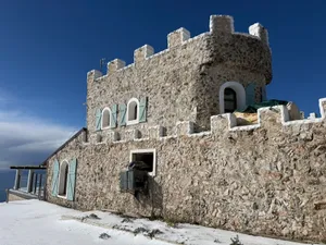 A stone building with castle-like features and blue shutters under a clear sky. jigsaw puzzle