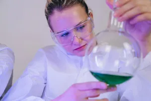 A female scientist closely examines a green solution in a laboratory setting, wearing protective gear. jigsaw puzzle