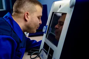 A man in a blue uniform interacting with a touchscreen device indoors. jigsaw puzzle