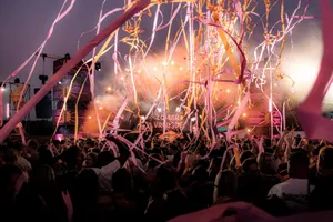 Crowd enjoying a vibrant festival with colorful ribbons and stage lights under a twilight sky. jigsaw puzzle