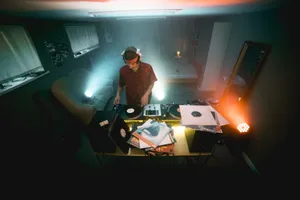 A DJ in an apartment mixing vinyl records in a dimly lit room with ambient lighting. jigsaw puzzle
