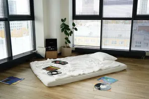 A minimalist apartment interior with a mattress on the floor surrounded by vinyl records and a record player. jigsaw puzzle