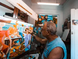 An elderly artist skillfully paints a colorful canvas in his studio, surrounded by vibrant artworks. jigsaw puzzle