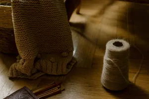 From above of handmade woolen blanket placed in wicker basket near various wooden knitting needles located on parquet floor with spool of thread jigsaw puzzle