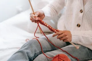 Crop unrecognizable female in trendy warm cardigan and jeans sitting on comfy bed and knitting with needles during weekend at home jigsaw puzzle