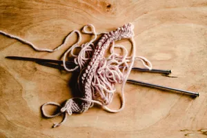 A close-up view of pink yarn and knitting needles on a wooden table, ideal for crafts and DIY themes. jigsaw puzzle